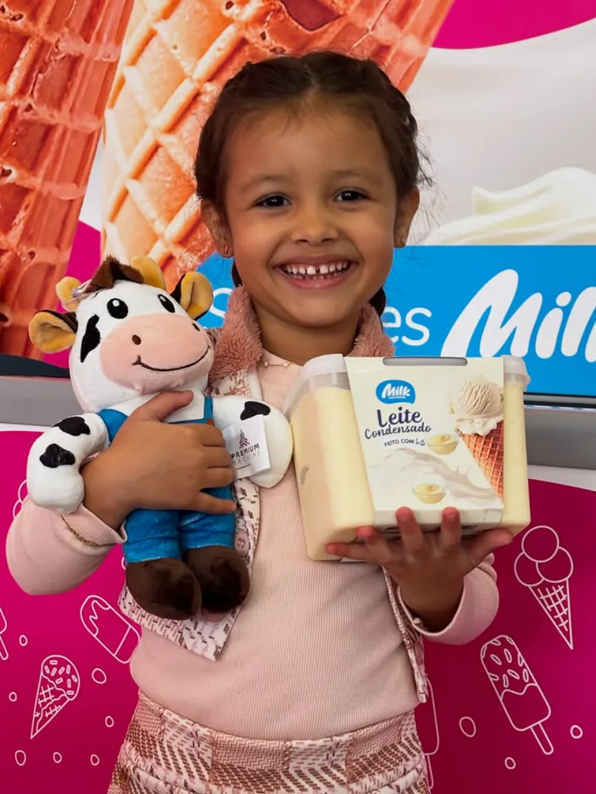 Menina sorrindo com pelúcia do mascote e pote de sorvete de leite condensado Milk