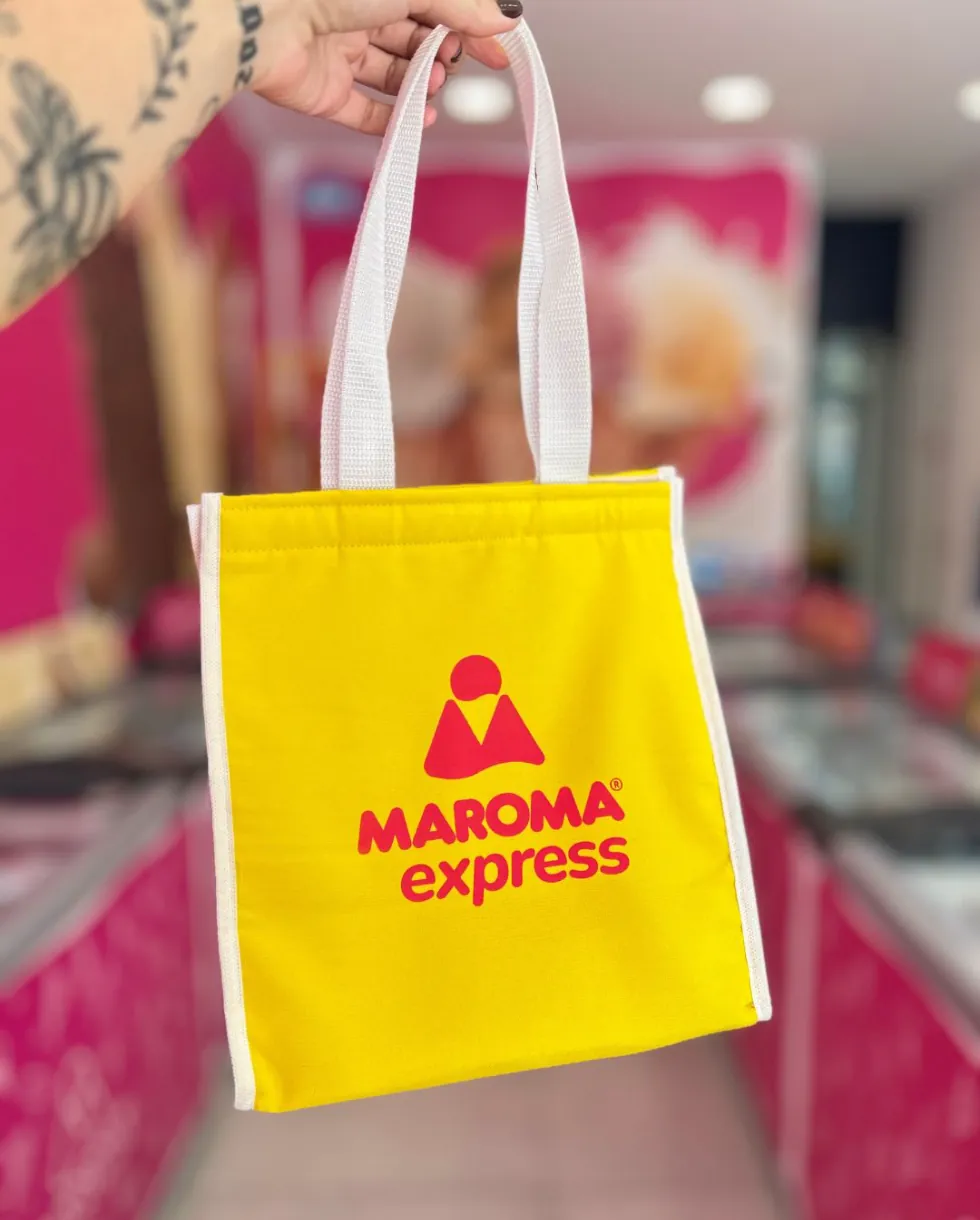 Sacola térmica amarela da Maroma Express segurada em frente à loja